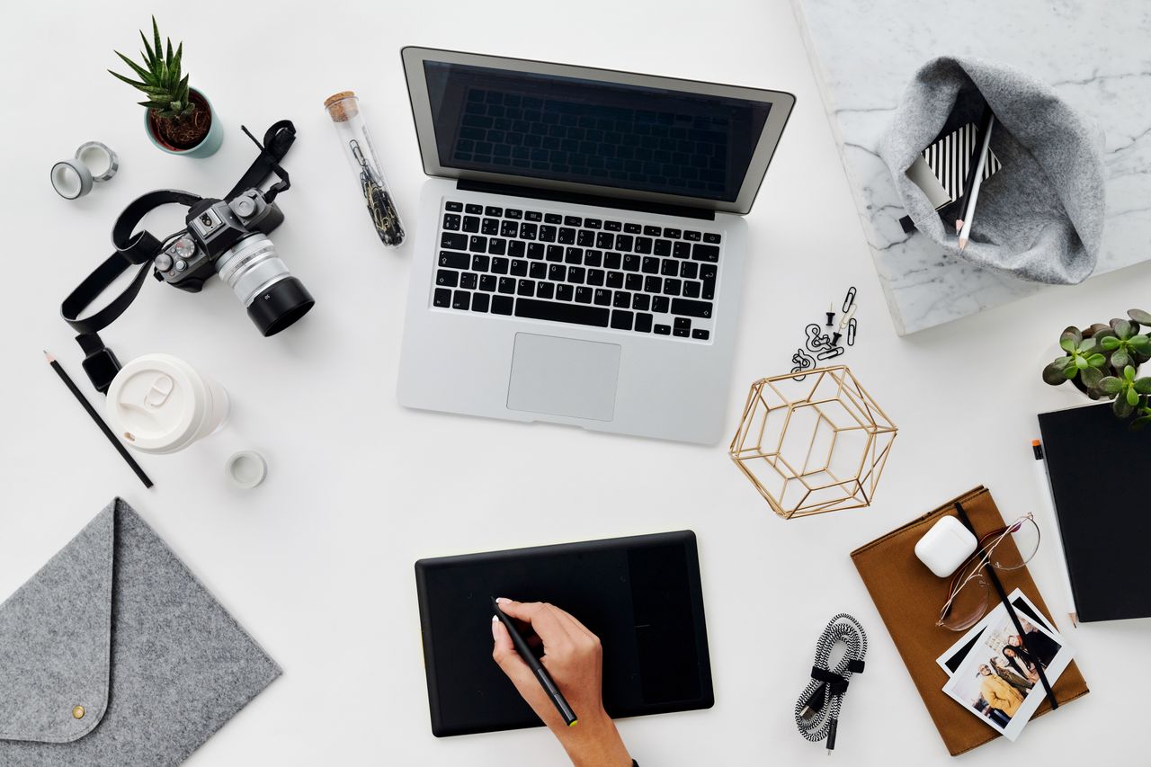 A stylish overhead view of a creative workspace featuring digital devices, drawing tablet, and stationery.