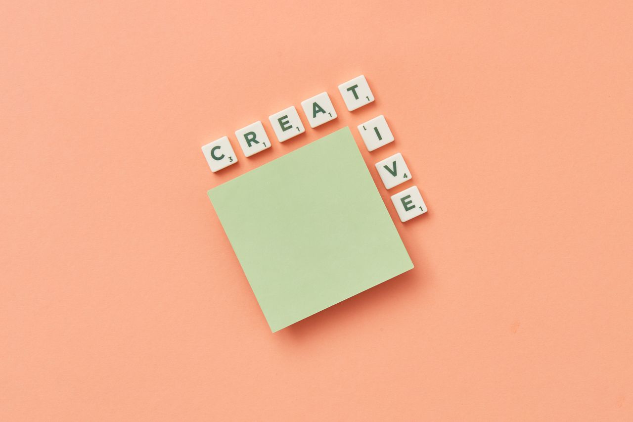 Offerings Minimalist creative concept with green sticky note and letter tiles on peach background.